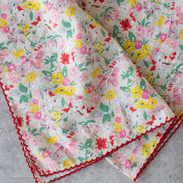 square cotton scarf in beige with allover dainty floral print in red, pink, yellow, and green and finished with rich red embroidered scallop trim, showing close up detail
