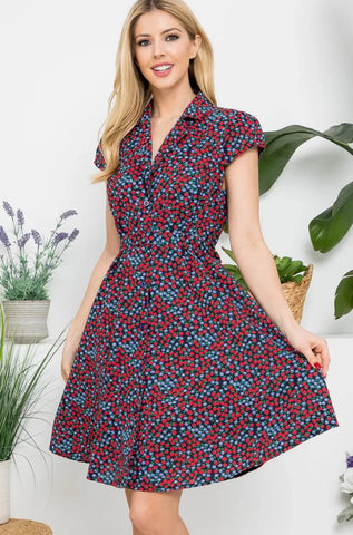 button-front closure dress in a black background ditzy print of red strawberries and blue flowers, featuring a notched collar v-neckline, princess seamed bodice, gathered shoulder cap sleeves, removable self sash belt, and just above the knee flared skirt, shown on model