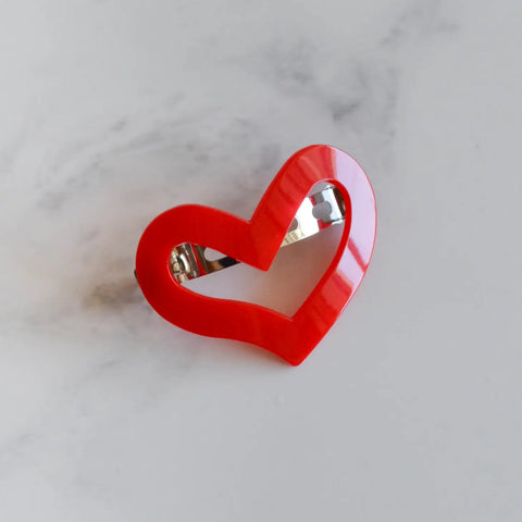 A plastic barrette in the shape of a red stylized heart with a pinch clip fastener on its back
