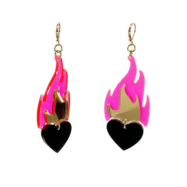 A pair of acrylic dangle earrings in the shape of a shiny black heart surrounded by a neon pink flame and mirrored gold inner flame