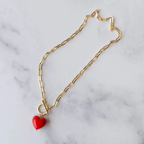 A shiny red heart pendant on a 17” gold metal paperclip chain link necklace with front toggle closure