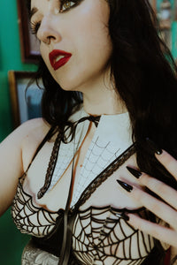A dagger-style detachable collar that is made of soft matte white mercerized cotton and has a black satin ribbon tie. The front of the collar has delicate black spiderweb embroidery and a black lace trim. Shown on a model in close up
