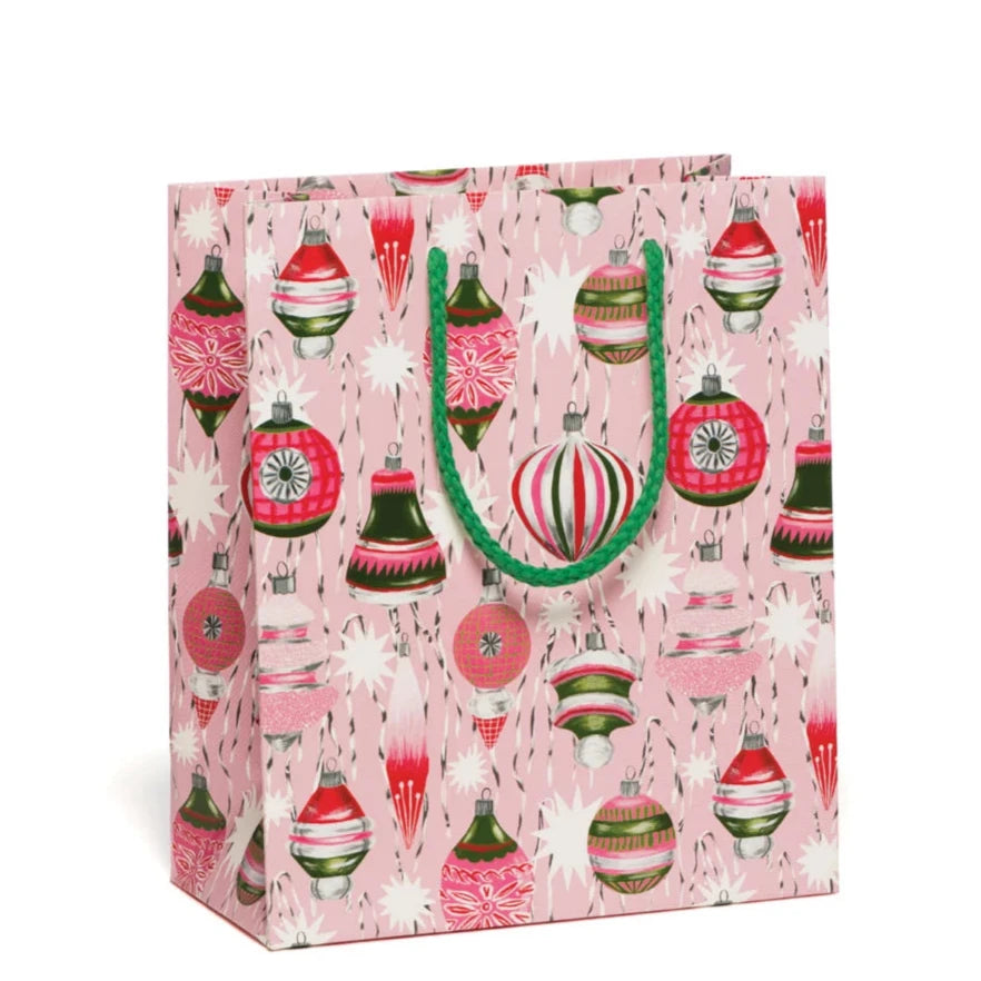 A gift bag with an allover print of beautiful red, green, and white vintage tree ornaments on a cotton candy pink background