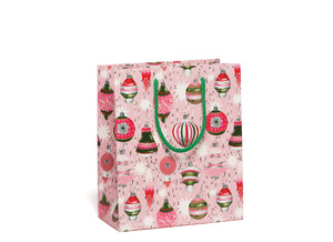 A gift bag with an allover print of beautiful red, green, and white vintage tree ornaments on a cotton candy pink background