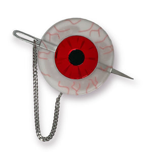 acrylic brooch in the shape of a bloodshot eye with bright red mirrored iris and a shiny mirrored sewing needle attached with a delicate curb style chain that can be placed right through the eye