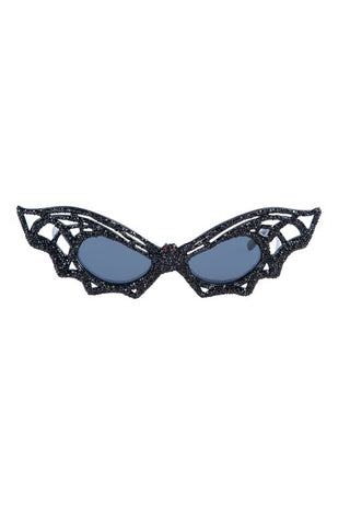 A pair of cat-eye style sunglasses in the shape of a bat with cutout details representing the bats' wings. The glasses are covered in black rhinestones with two red rhinestones as the bat's eyes across the bridge of the glasses.