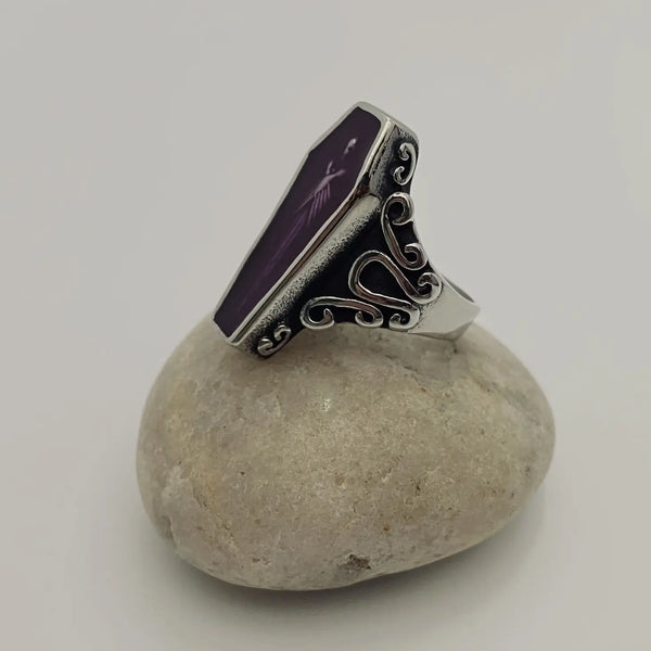 stainless steel ring depicting a vampire encased in translucent purple acrylic resin, at rest in his coffin, shown side view