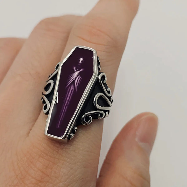 stainless steel ring depicting a vampire encased in translucent purple acrylic resin, at rest in his coffin, shown on a finger