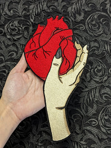 embroidered patch of a witchy hand with long & pointy black fingernails holding a large red anatomical heart