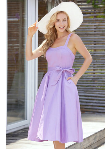 A model wearing a sleeveless with dress with a fitted sweetheart neckline princess seamed bodice with adjustable straps, removable self sash belt, swingy gathered full circle just below the knee length skirt