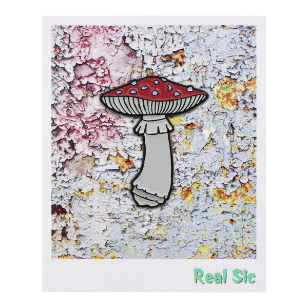 shiny black enameled pin of the classic red and white spotted amanita muscaria mushroom. Shown on its cardboard packaging 
