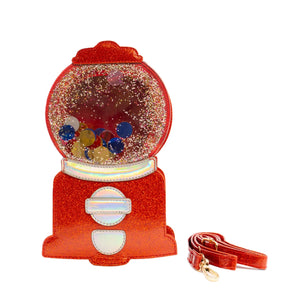 A red glittery vinyl purse in the shape of a gumball machine with a translucent window, glitter, and movable sequin “gumballs”. Next to it is the removable crossbody strap