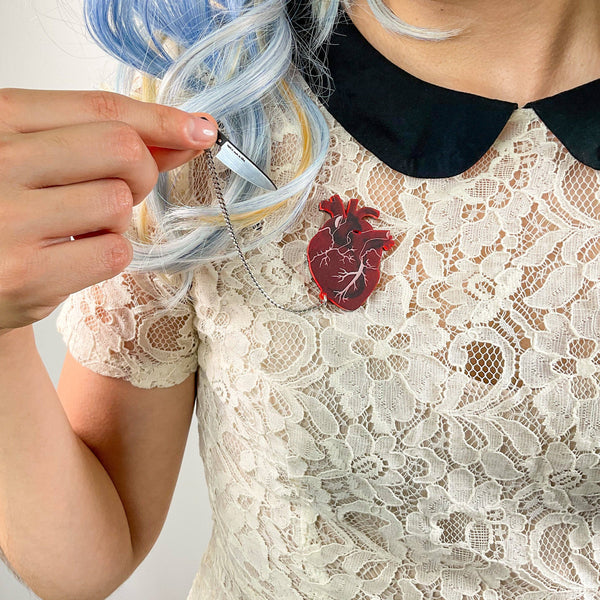 frosty translucent red anatomical heart layered over black laser cut acrylic brooch with removable tiny silver metal chain tethered black & metallic silver chef knife, shown on model