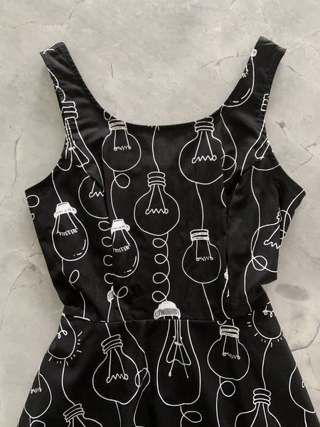 black cotton fit & flare sleeveless mini dress with white allover novelty print of assorted Edison style lightbulbs, shown close up flatlay