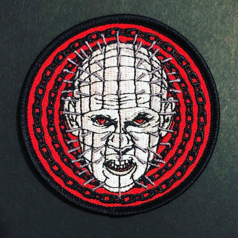 A round embroidered patch of Pinhead from the movie Hellraiser in front of a red and black concentric chainlink background