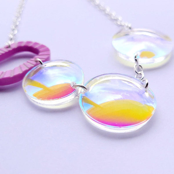 acrylic statement necklace from Sugar & Vice features a bubblegum pink bubble wand and three clear iridescent domed bubbles linked together on a shiny silver metal chain