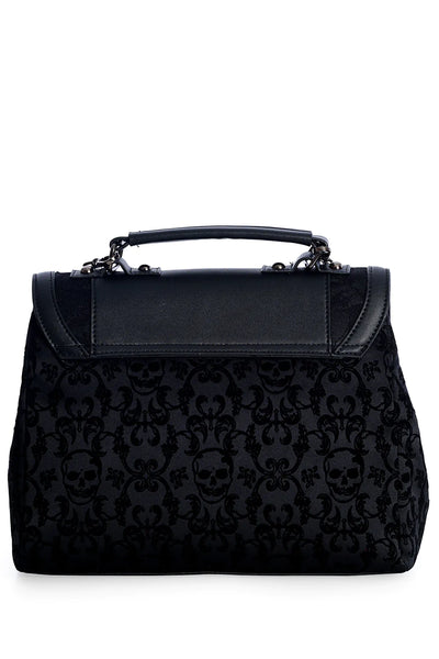 A black matte vinyl handbag with damask skull pattern body and a scalloped front flap with a bow and black lace detailing. The bag has a black matte vinyl hand strap and a gunmetal chain shoulder strap. The back of the purse