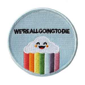An embroidered patch with a light blue background and a smiling cartoon cloud with a rainbow underneath. The words “We’re all going to die” are written in black above the cloud 