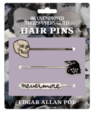 A set of three metal Bobby pins with Edgar Allan Poe themed charms on the end of each pin- a skull, a raven, and “Nevermore” written in black script. Shown on its cardboard packaging 