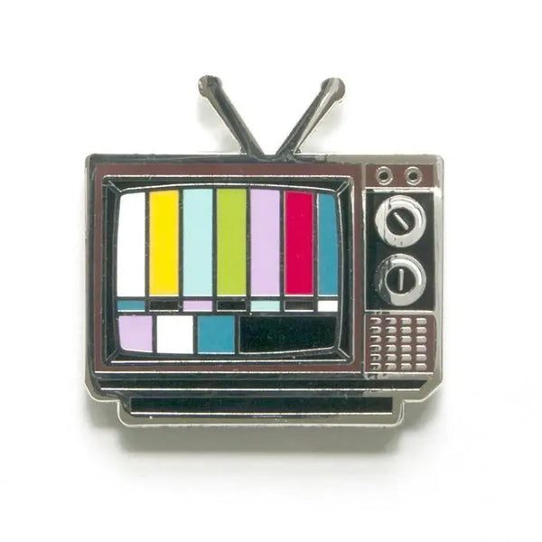 A silver metal enamel pin of a black and brown old fashioned tv with antenna and a multicolor test pattern on its screen