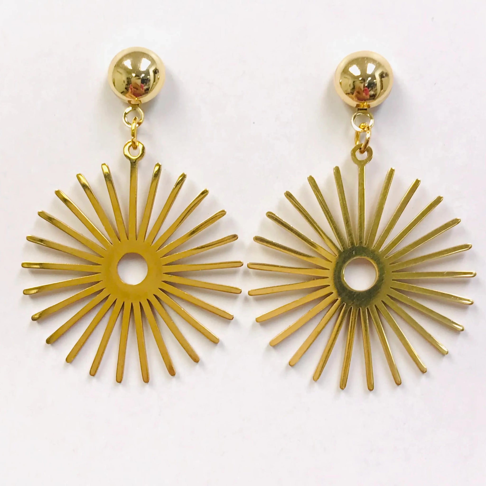 A pair of gold metal drop earrings with a large starburst attached to a post backing
