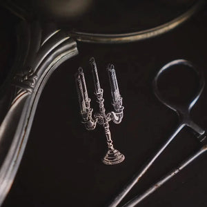 An enamel pin of a silver and black candelabra with 5 candles