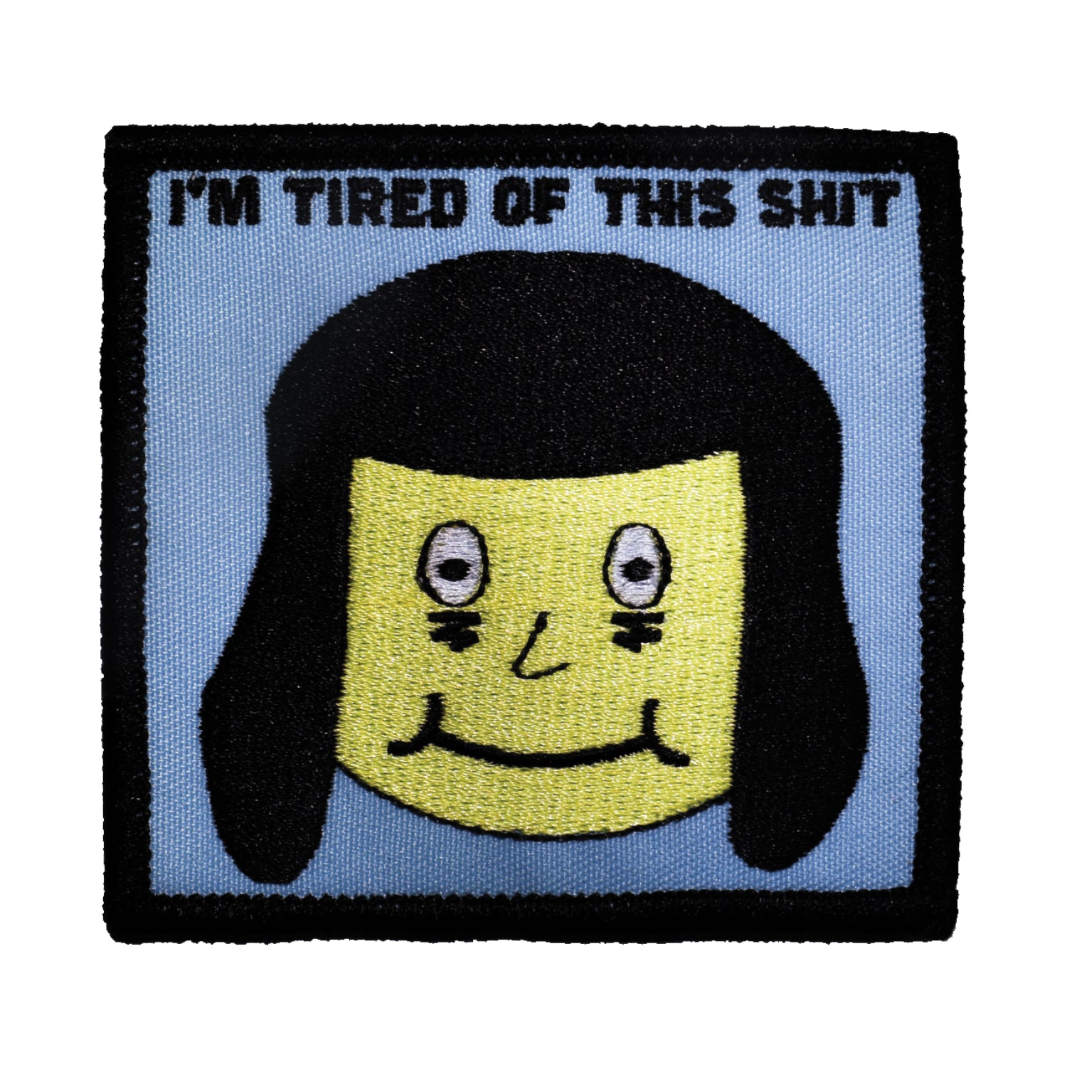 A square cotton twill embroidered patch with a face of a person with exaggerated bags under their eyes and a nervous smile with the caption “I’M TIRED OF THIS SHIT” written in black above their heac