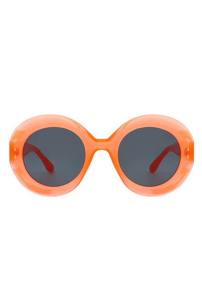 A pair of semi translucent orange oval sunglasses with smoke lenses and gold detailing on the temples