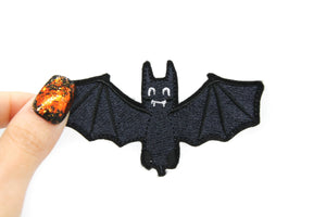 embroidered patch of a happy cartoon bat with a smile on its face. The bat is black with white eyes and mouth