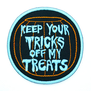 A round black cotton twill patch with bright blue border of an orange Halloween candy bowl with the caption “Keep your tricks off my treats” in blue drippy Halloween style lettering in the middle 