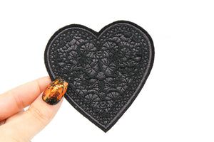 embroidered patch of a heart with lace-style detail in grey and black stitching and a black border