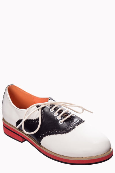 A pair of black and white faux leather lace up saddle shoes with a red sole.