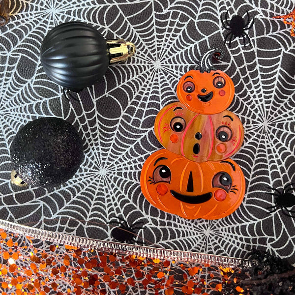 "Stack O'Jacks" trio of sweet-faced jack-o'-lanterns layered laser cut resin brooch, shown against spiderweb background