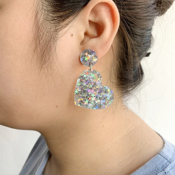 heart-shaped acrylic drop earring filled with iridescent starburst-shaped pieces of glitter, shown on model