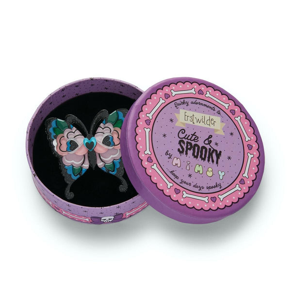 "Fright of the Butterfly" pink, blue, green, and glitter black layered resin brooch, shown in illustrated round box packaging