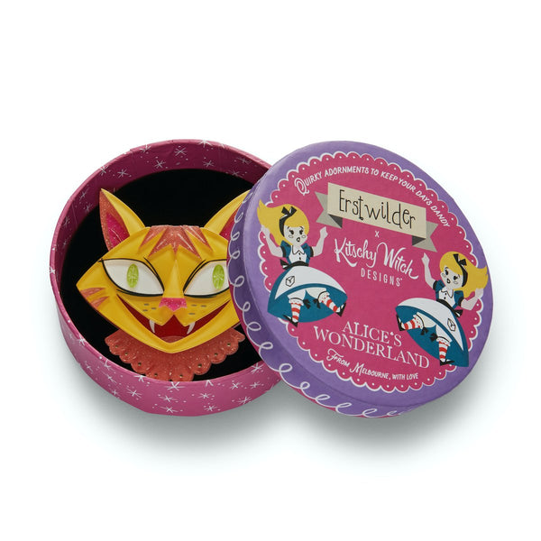 The Cheshire Cat yellow and pink with green eyes layered resin brooch, shown in illustrated round box packaging