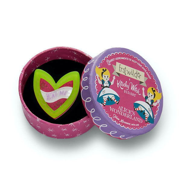 green and hot pink heart-shaped cake with white "EAT ME" banner label layered resin brooch, shown in illustrated round box packaging