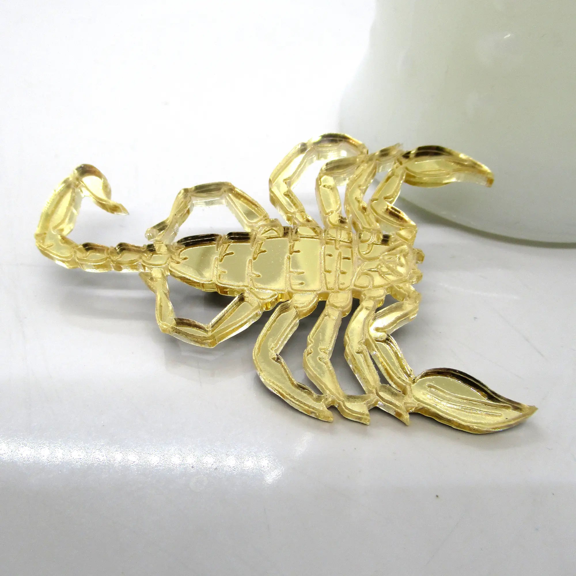 A laser cut gold mirrored acrylic brooch of a scorpion with etched detailing