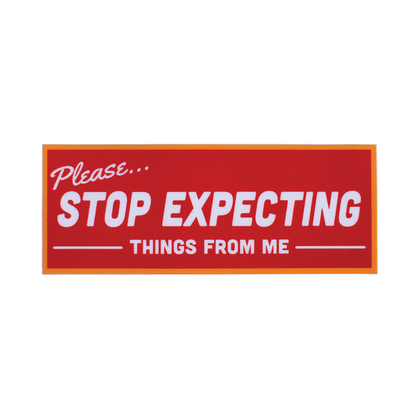 A rectangular vinyl sticker with an orange border that is meant to look like a retro storefront sign. It reads “Please… Stop expecting things from me” in white. The background is a red-orange 