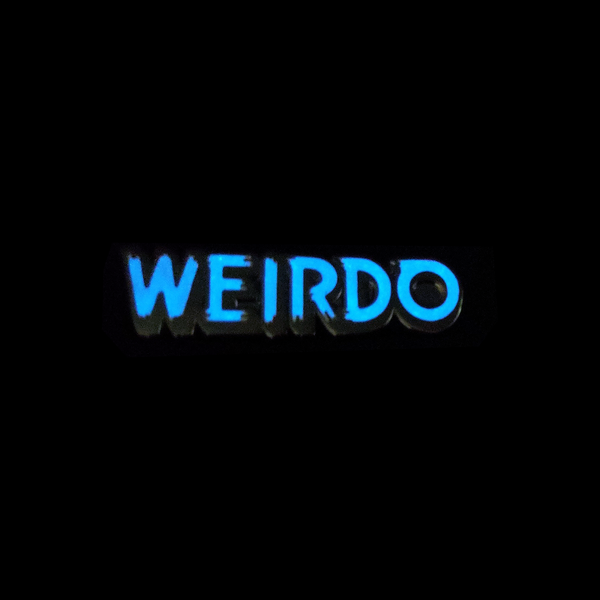 "WEIRDO" text glow in the dark white enameled gunmetal finish metal lapel pin, shown glowing blue against a black background