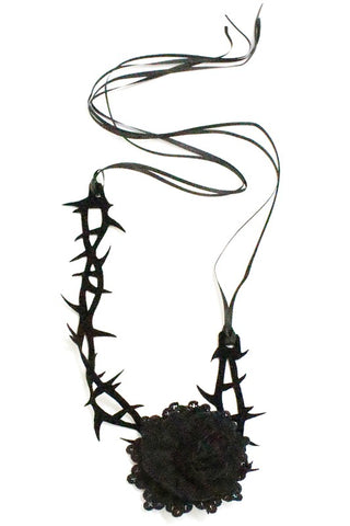 choker is made of black flocked fabric laser cut into a thorn pattern with an attached lace black rose decoration off-center. A double piece of satiny black ribbon is tied to each end of the choker