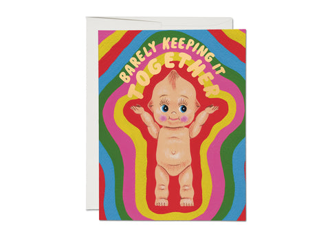 Greeting card of a smiling kewpie doll with outstretched arms and the text “Barely Keeping It Together” in metallic gold lettering. On a swirled pink, yellow, red, blue, and green background