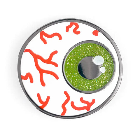 A silver metal enamel pin of a bloodshot eyeball with bright green glittery iris