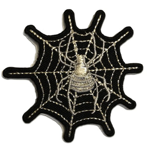 An embroidered patch of a white and silver spider in front of a silver spider web on a black background