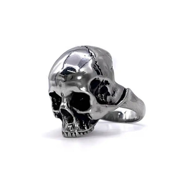 A stainless steel ring of a detailed skull on a solid stainless steel band. Shown at a 3/4 angle facing the left to show detail 