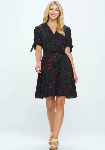 button-front shirtwaist dress in black with allover red heart dot print, featuring notched collar v-neckline, puffed shoulder short sleeves finished with a tie closure detail, self sash belt, and just above the knee flared skirt, shown on model