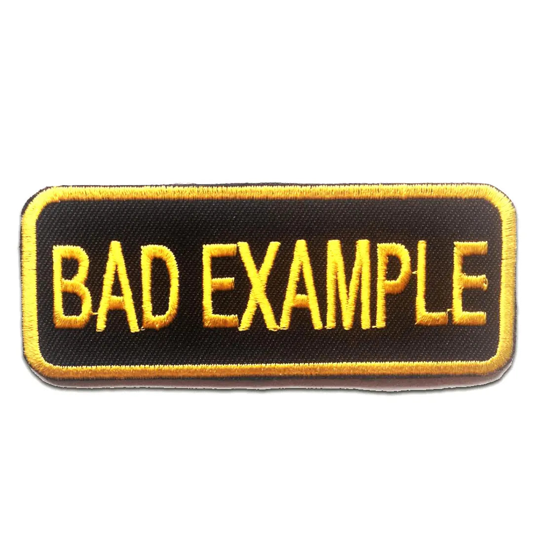 A rectangular name tag style patch that says “BAD EXAMPLE” in yellow embroidered letters on a black background. The border around the patch is also embroidered yellow