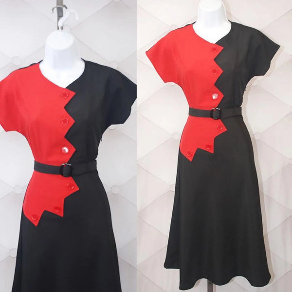 A 40s style short sleeved dress with sawtooth style color blocking in red and black down the front. It has dolman-style cap sleeves, red buttons down the length of the dress, and a matching fabric belt in black with a plastic buckle. Shown on a dress form 