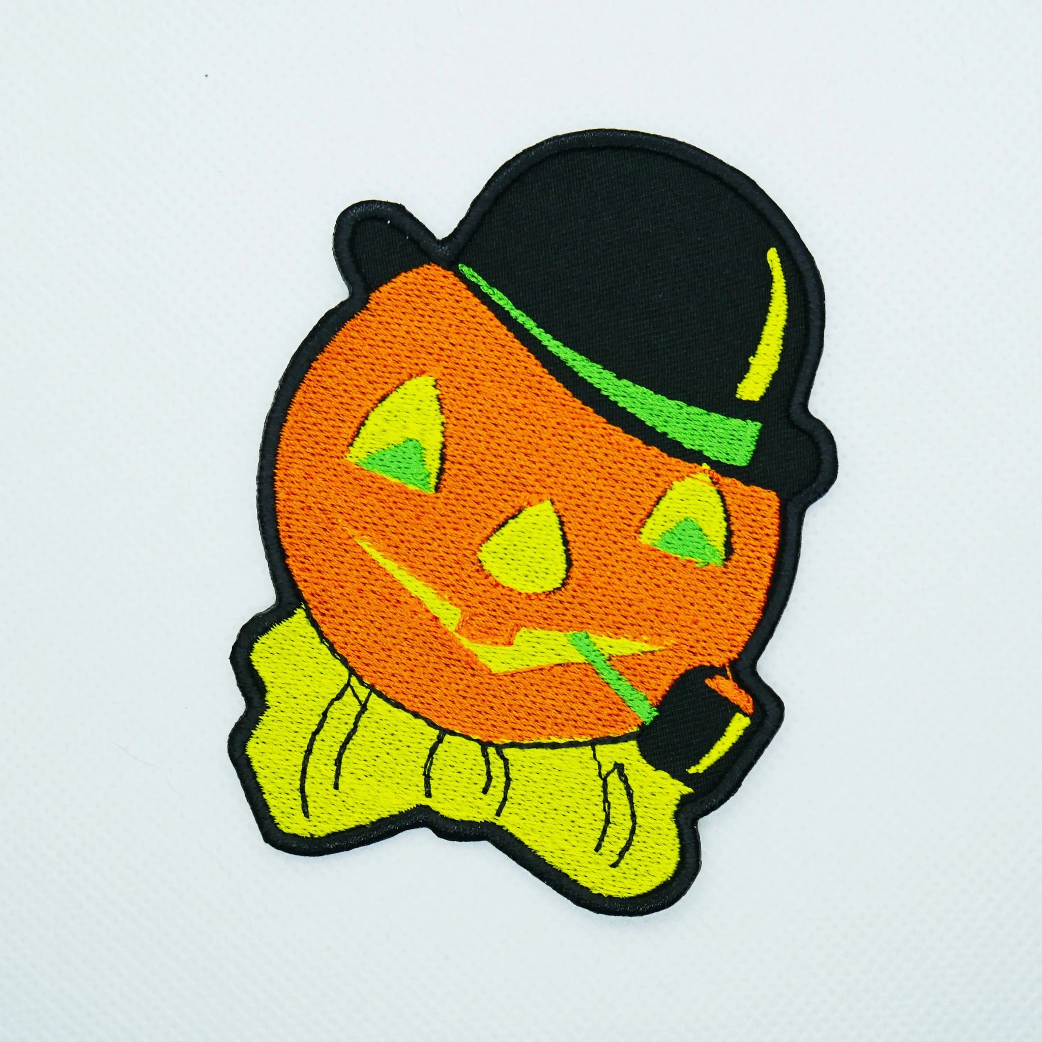 A cotton twill embroidered patch of a vintage Halloween decoration style carved pumpkin with a bowler hat, bow tie and corncob pipe