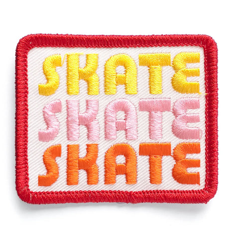 A rectangular embroidered patch with the word SKATE repeated three times in yellow, pink, and orange retro font on an off white background. The patch has a bright red border